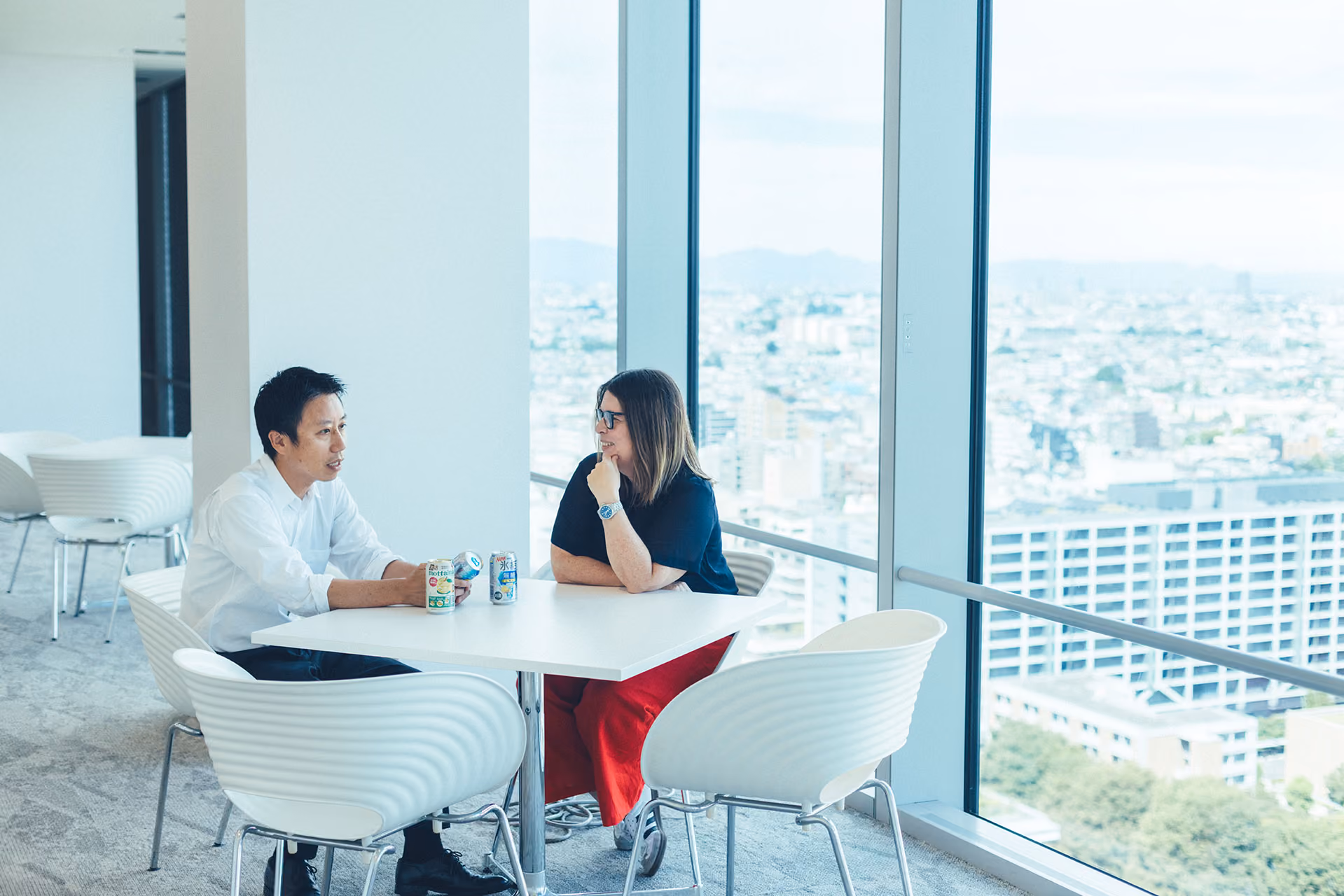 Takahiro Matsumura and Rachel Ellerm are sitting at a table next to a large window and having a conversation. Three cans of KIRIN HYOKETSU are on the table, and Takahiro Matsumura is holding one of them.