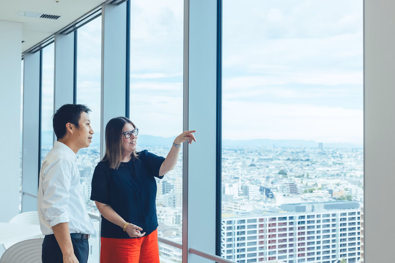 Rachel Ellerm is pointing at the view outside a large window, and Takahiro Matsumura is looking at it, too, as they engage in conversation.