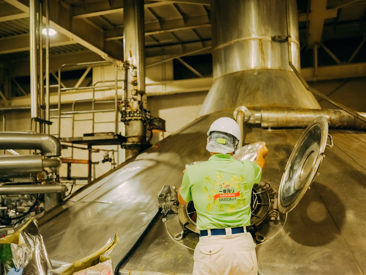 A figure seen from behind adding frozen hops to a beer mash kettle