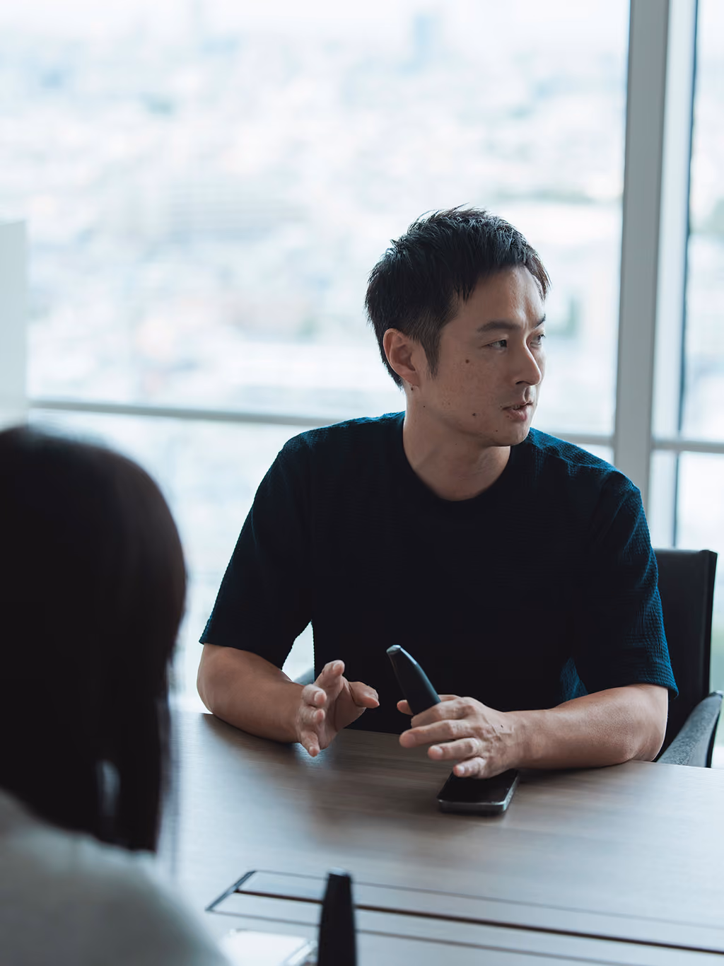 Sho Tsugawa speaking with Lumen in one hand, with a window behind him