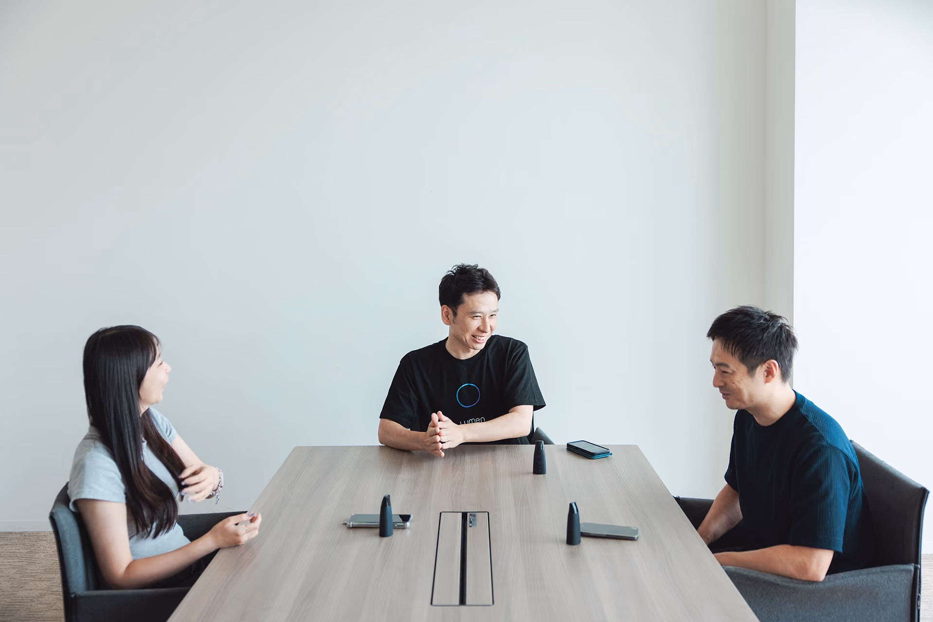 Three people conversing around a desk and Lumens